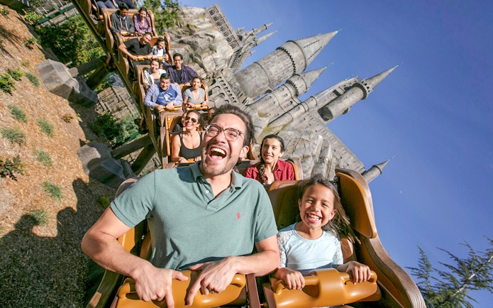 Tourists enjoying a roller coaster ride at Universal Studios Hollywood with Hogwarts Castle in the background.