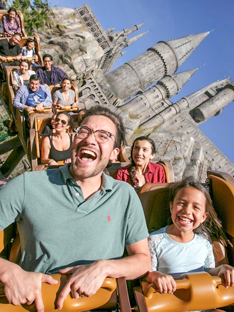 Tourists enjoying a roller coaster ride at Universal Studios Hollywood with Hogwarts Castle in the background.
