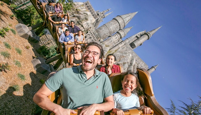 Tourists enjoying a roller coaster ride at Universal Studios Hollywood with Hogwarts Castle in the background.