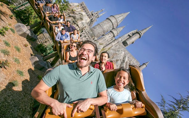 Tourists enjoying a roller coaster ride at Universal Studios Hollywood with Hogwarts Castle in the background.