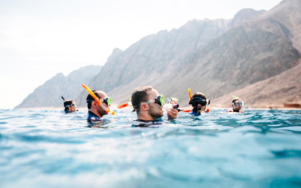 Friends snorkeling in clear sea near rocky coastline.