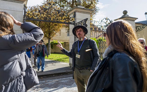 Tour guide explaining to tourists in front of Prague Castle gate.