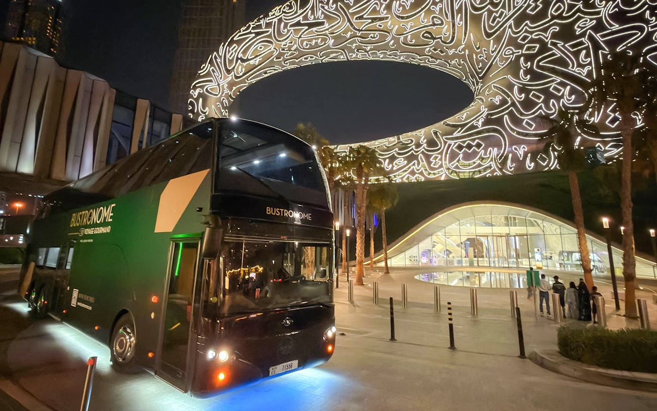 Bustronome restaurant bus parked near the illuminated Museum of the Future in Dubai.