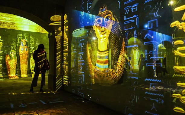 Ancient Egyptian artifacts and hieroglyphs projected in a dimly lit exhibit space.
