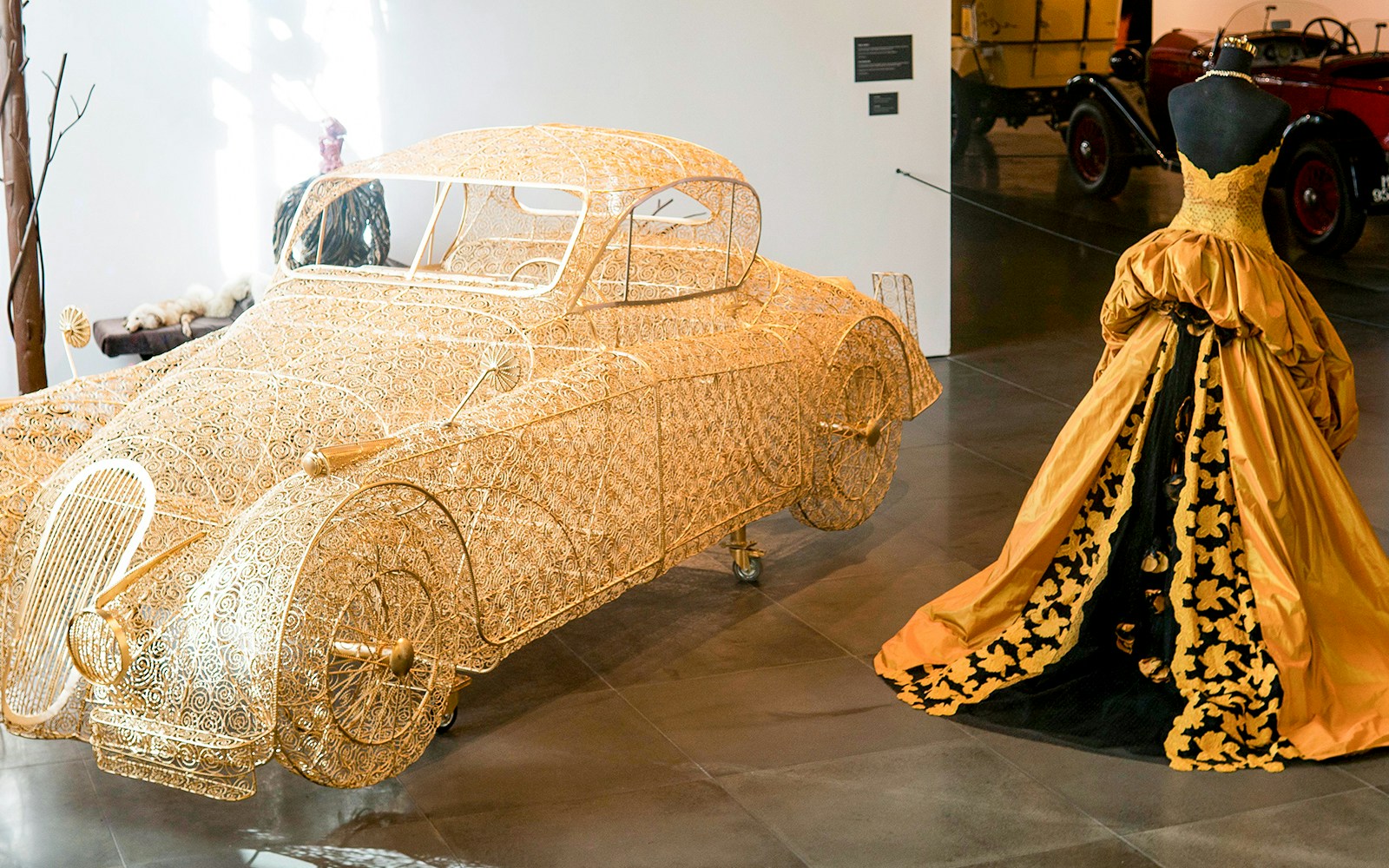 Golden wire car sculpture and vintage gown at Malaga Automobile & Fashion Museum.