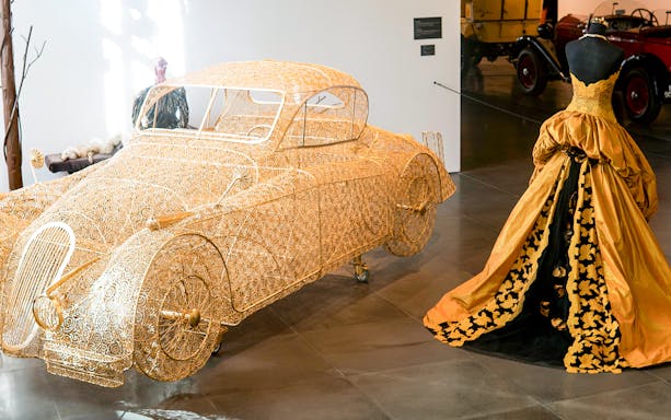 Golden wire car sculpture and vintage gown at Malaga Automobile & Fashion Museum.