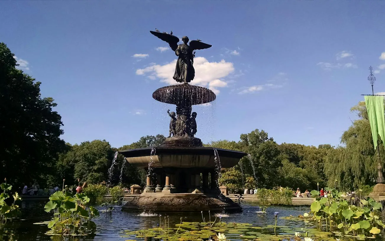 Bethesda Fountain in Central Park, New York, surrounded by greenery and water lilies.