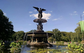 Bethesda Fountain in Central Park, New York, surrounded by greenery and water lilies.