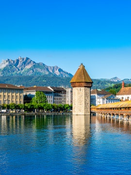 Chapel Bridge and Pilatus Mountain in Lucerne, Switzerland, under clear blue sky.