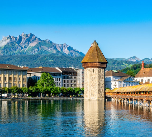 Chapel Bridge and Pilatus Mountain in Lucerne, Switzerland, under clear blue sky.