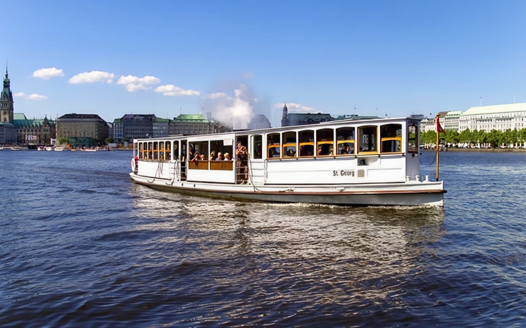 Historic steamboat on Hamburg's Alster Lake with city skyline in background.
