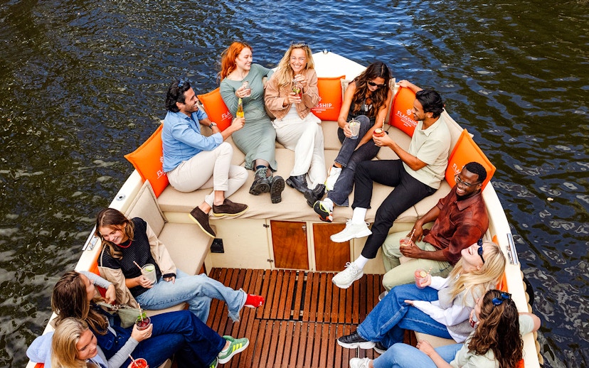 Guests enjoying drinks on a luxury open boat cruise in Amsterdam canal.