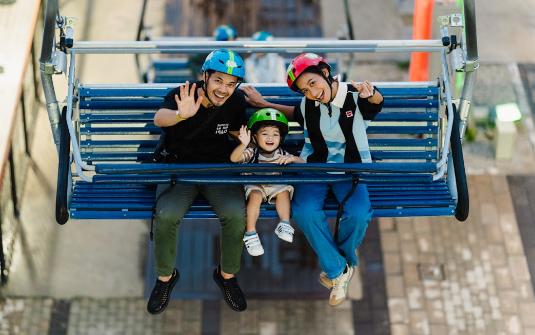 Family on chair lift at Skyline Luge Kuala Lumpur, smiling and waving.