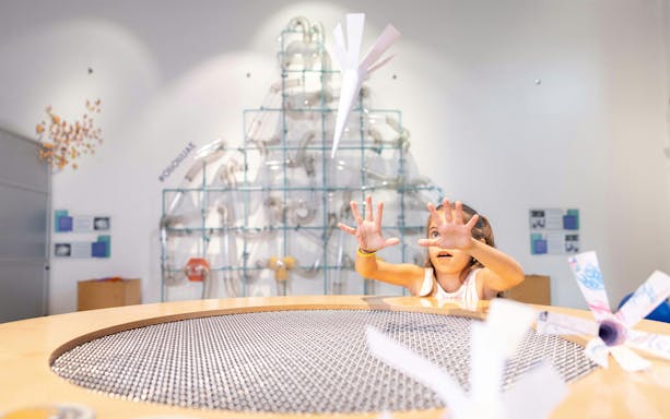 Child interacting with paper plane exhibit at OliOli Children's Museum.