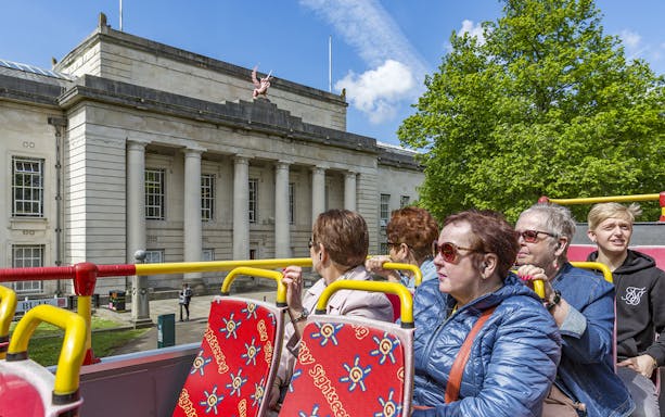 Cardiff hop-on hop-off bus passing National Museum Cardiff with tourists.