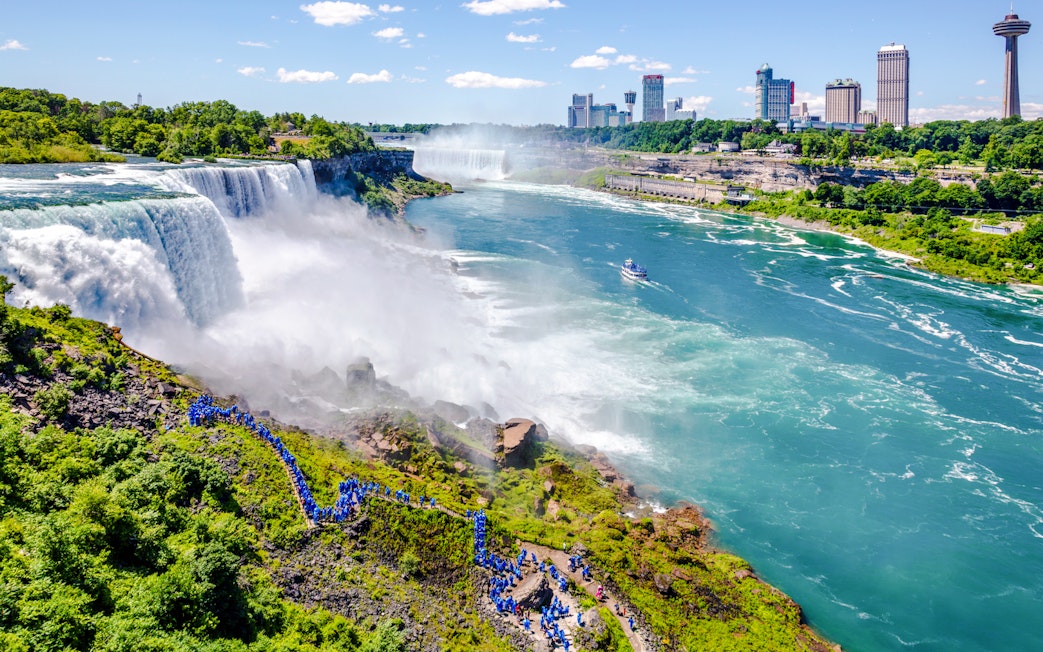 Aerial view of Niagara Falls with tourists in blue ponchos and a boat on the river.