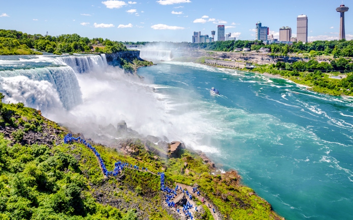 Aerial view of Niagara Falls with tourists in blue ponchos and a boat on the river.