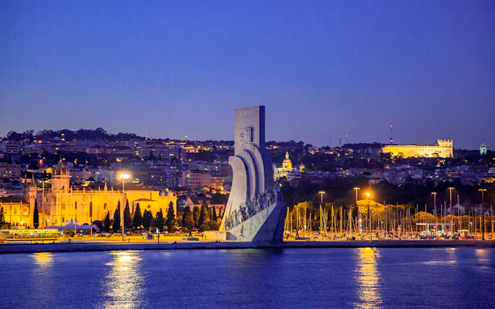 Lisbon night view with Monument to the Discoveries and illuminated cityscape.