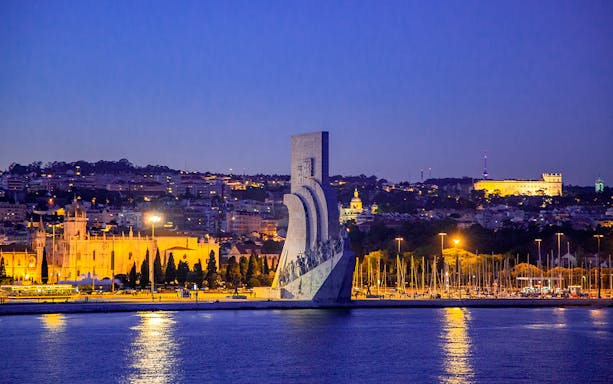 Lisbon night view with Monument to the Discoveries and illuminated cityscape.