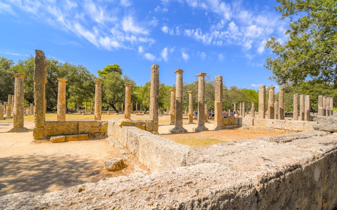 Ruins of the Palaestra wrestling school at ancient Olympia, Greece, with stone columns and trees.