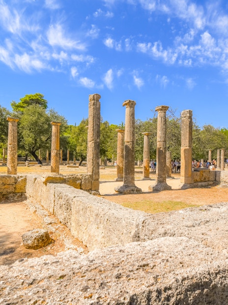 Ruins of the Palaestra wrestling school at ancient Olympia, Greece, with stone columns and trees.