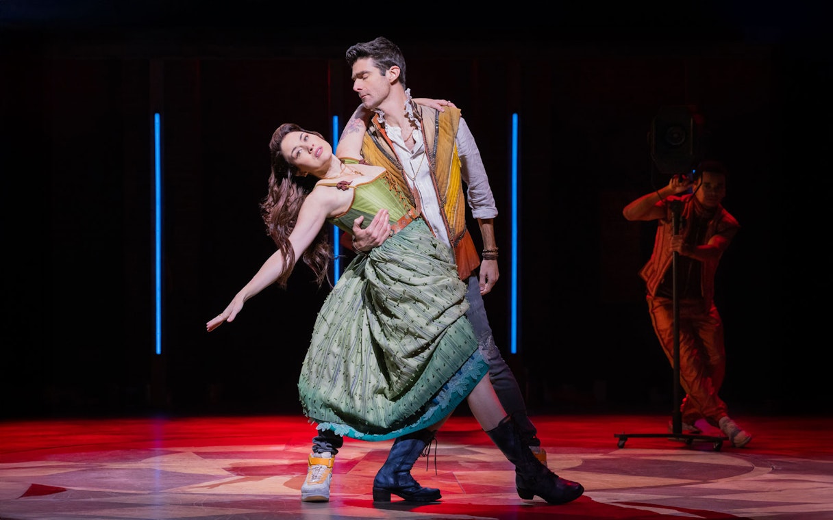 Performers dancing on stage in the musical "& Juliet" with dramatic lighting.
