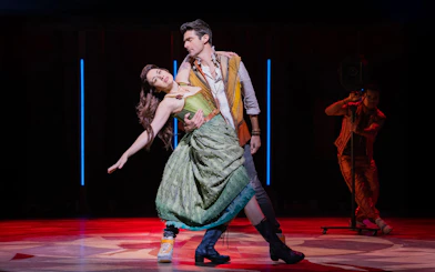 Performers dancing on stage in the musical "& Juliet" with dramatic lighting.