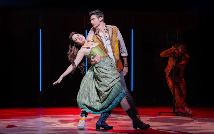Performers dancing on stage in the musical "& Juliet" with dramatic lighting.