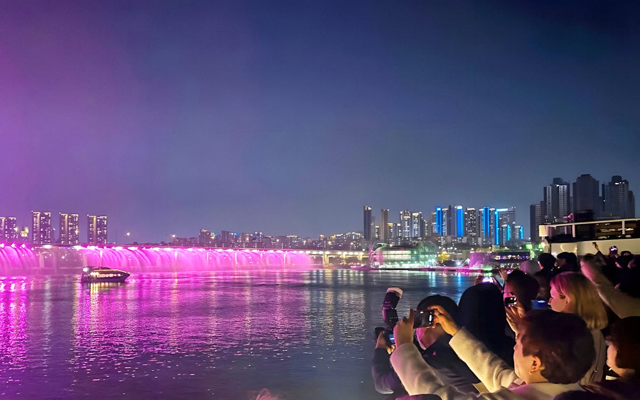 Night view of Han River cruise with illuminated bridge and city skyline in Seoul.