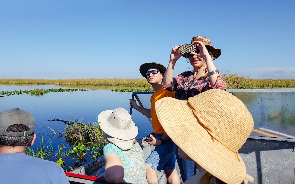 Guests photographing scenery on airboat during National Park tour.
