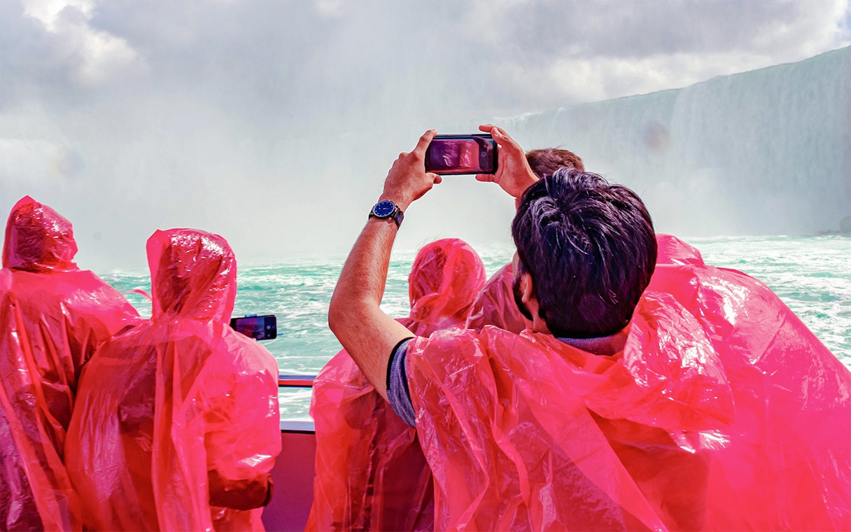 Passengers in red ponchos on Hornblower Cruise at Niagara Falls, Canada, taking photos.