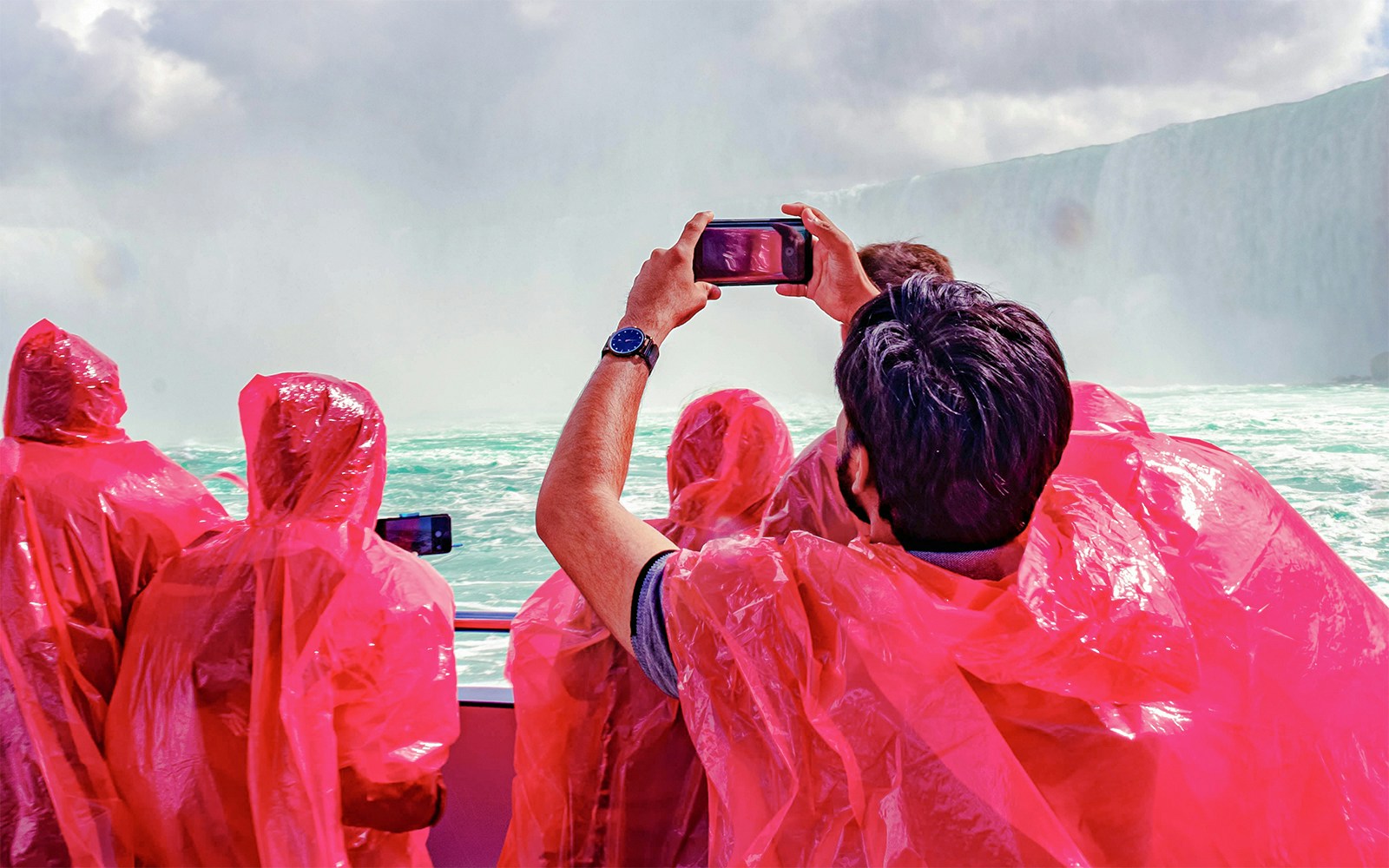 Passengers in red ponchos on Hornblower Cruise at Niagara Falls, Canada, taking photos.