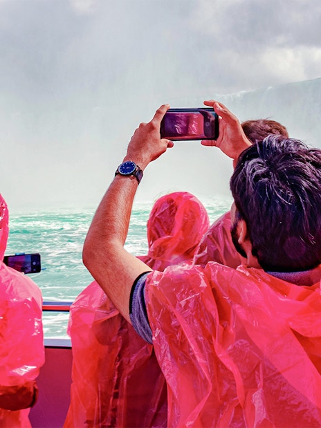 Passengers in red ponchos on Hornblower Cruise at Niagara Falls, Canada, taking photos.