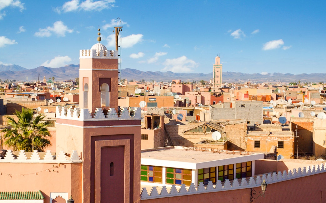 Rooftop view of Medina of Marrakech with minarets and Atlas Mountains in the background.
