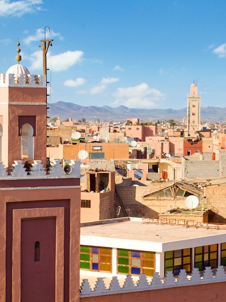 Rooftop view of Medina of Marrakech with minarets and Atlas Mountains in the background.
