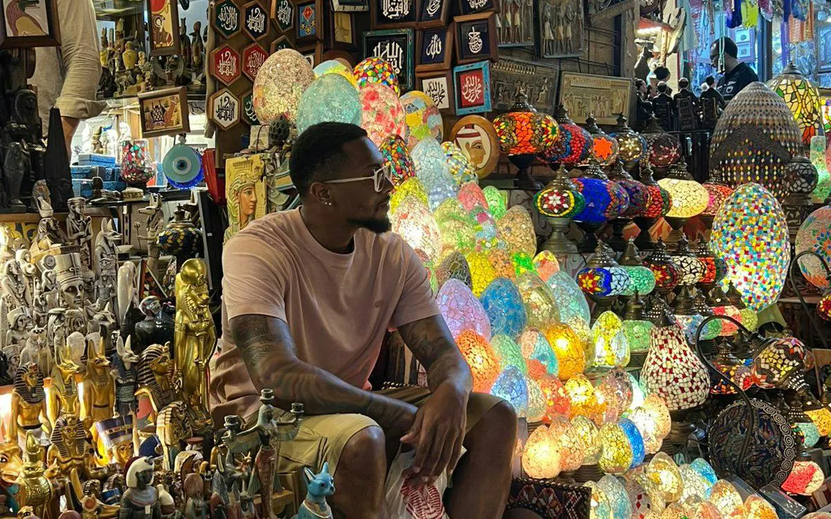 Man sitting among colorful lamps and souvenirs at Khan El Khalili market in Cairo.