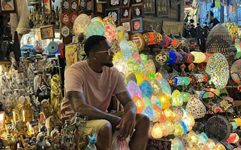 Man sitting among colorful lamps and souvenirs at Khan El Khalili market in Cairo.