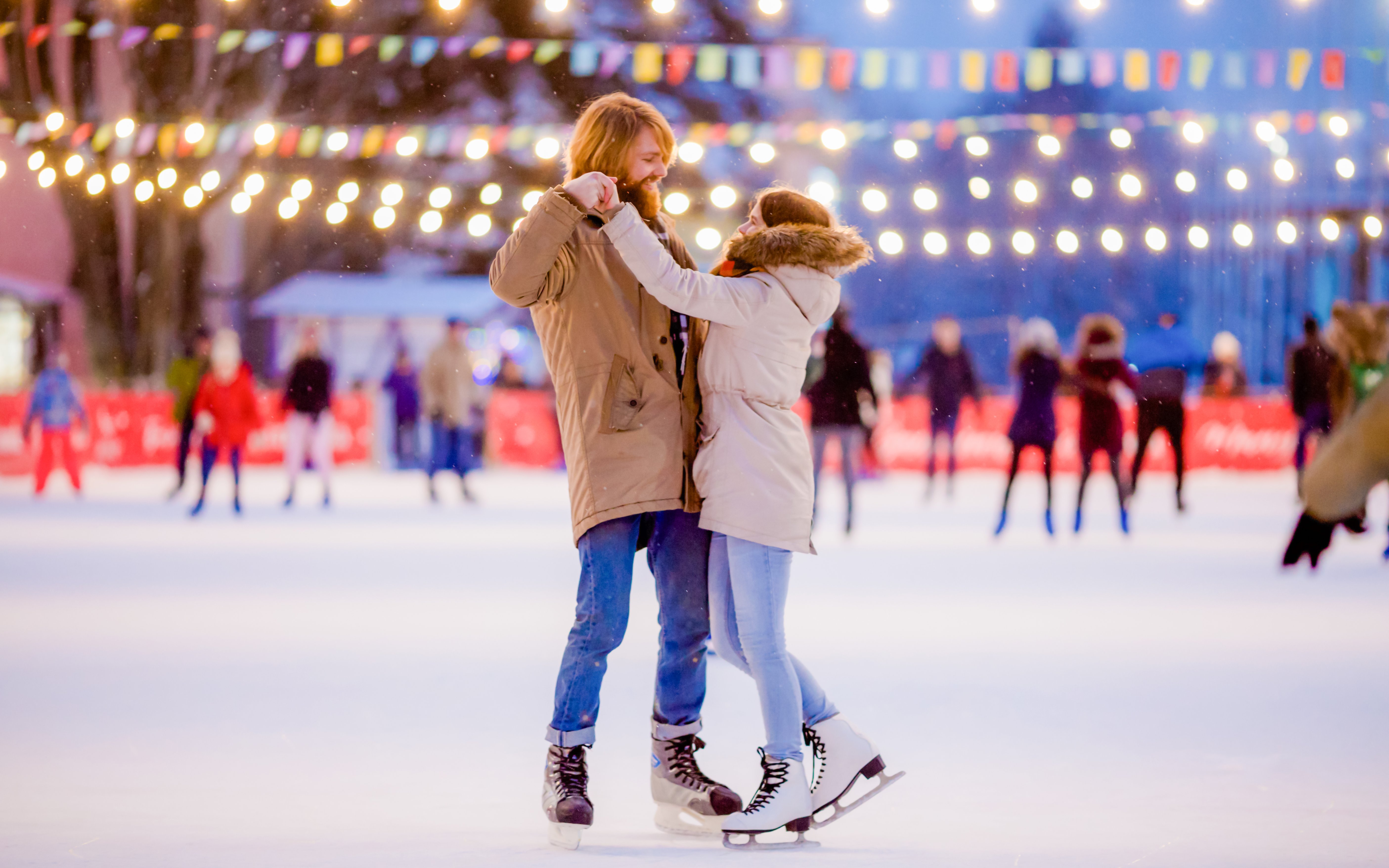 Couple ice skating under festive lights at night.