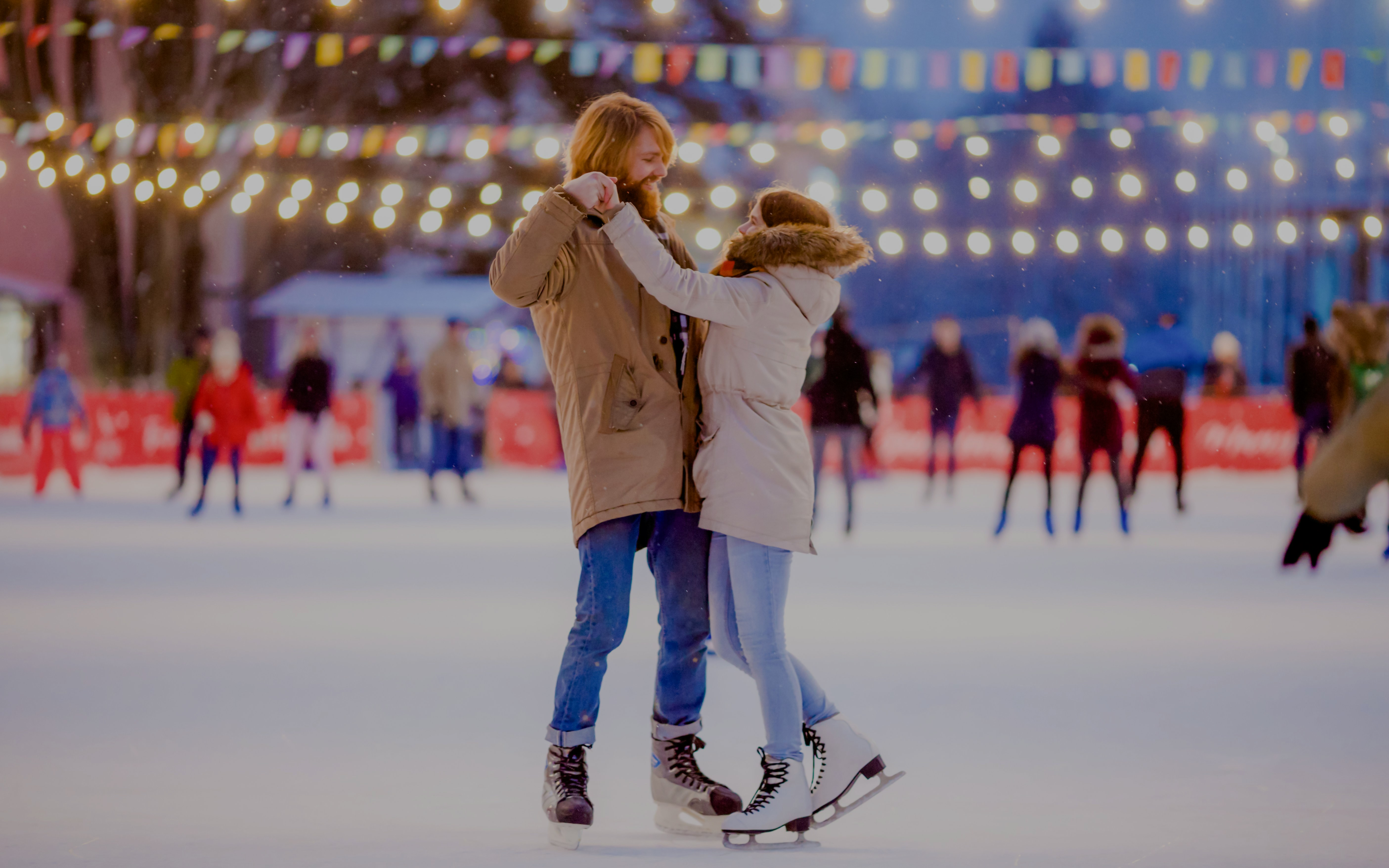 Couple ice skating under festive lights at night.