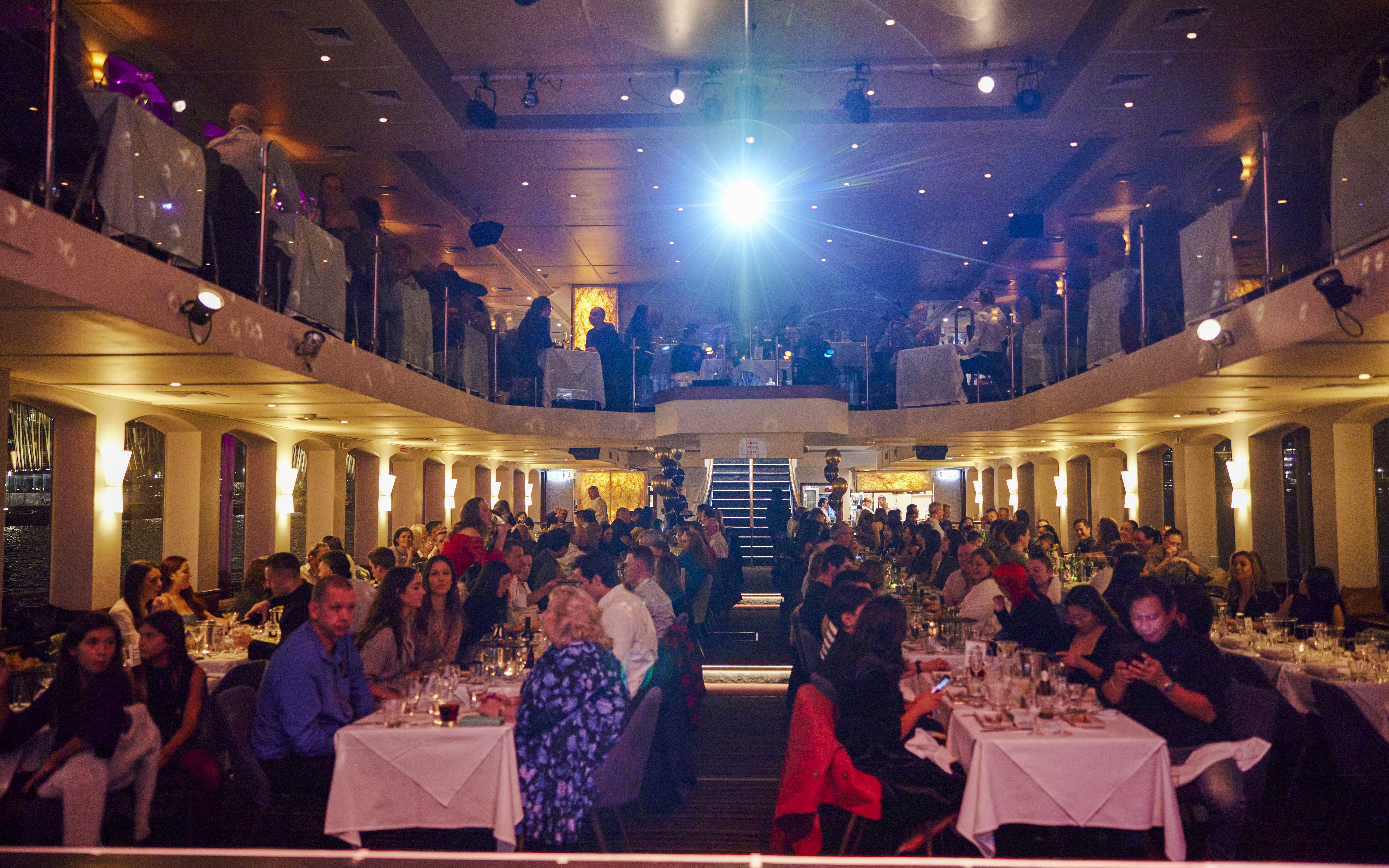 Dinner guests seated on a Showboat Vivid Sydney cruise enjoying a live cabaret performance.