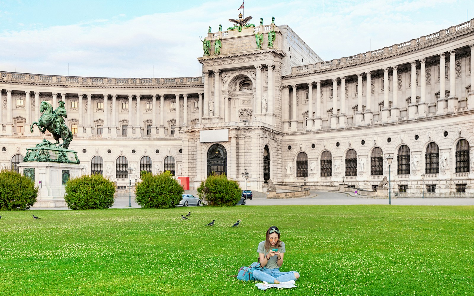 Woman sitting on lawn with Hofburg Palace in Vienna in the background.