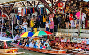 Vendors selling goods at Damnoen Saduak Floating Market with tourists in boats.