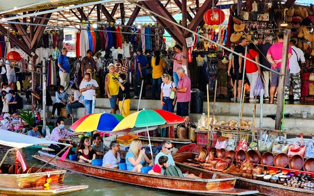 Vendors selling goods at Damnoen Saduak Floating Market with tourists in boats.