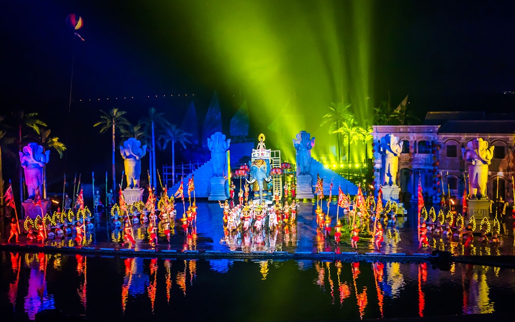 Performers in colorful costumes at Hoi An Memories Show, Vietnam, with vibrant lights and statues.