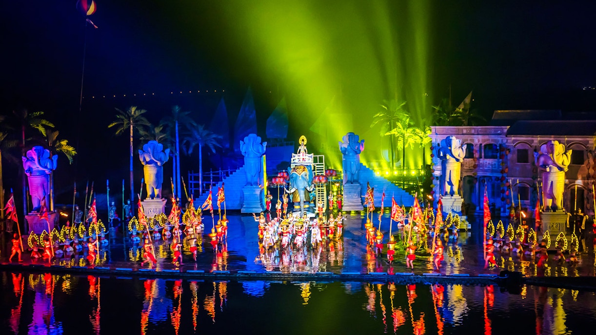 Performers in colorful costumes at Hoi An Memories Show, Vietnam, with vibrant lights and statues.