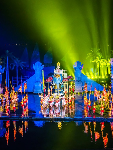 Performers in colorful costumes at Hoi An Memories Show, Vietnam, with vibrant lights and statues.