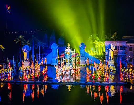 Performers in colorful costumes at Hoi An Memories Show, Vietnam, with vibrant lights and statues.