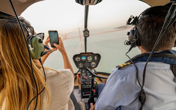 Helicopter cockpit view of Lisbon coastline with bridge in background.