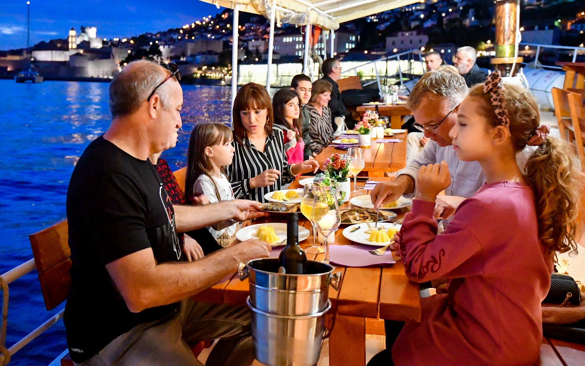 Guests dining on a dinner cruise in Dubrovnik with city lights in the background.