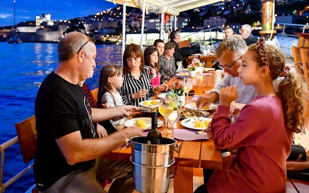 Guests dining on a dinner cruise in Dubrovnik with city lights in the background.